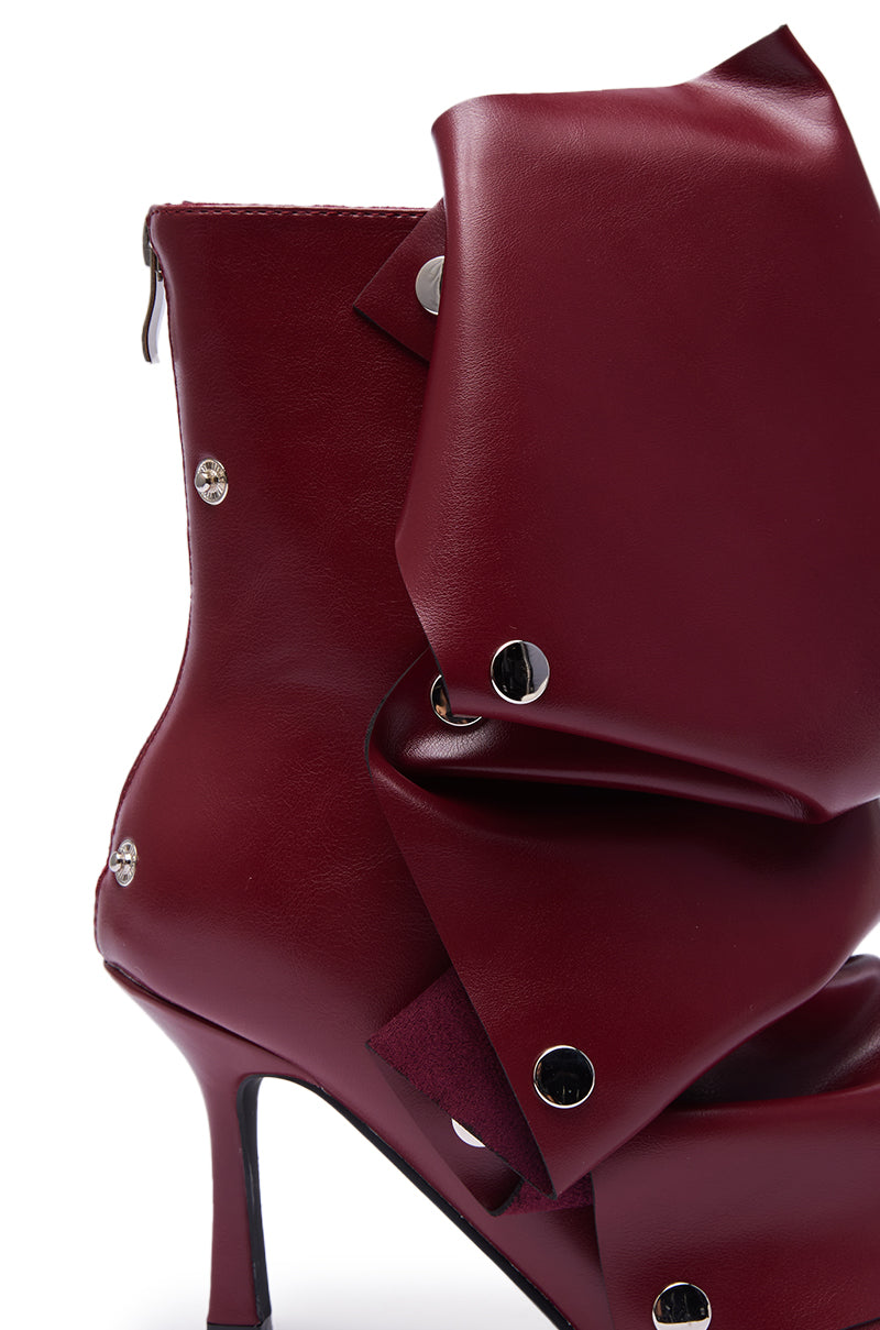 The AZALEA WANG BIRDSONG BURGUNDY SNAP OPEN TOE STILETTO BOOTIE showcases rich burgundy leather, folded layered panels with silver studs, and a back zipper for stylish flair.