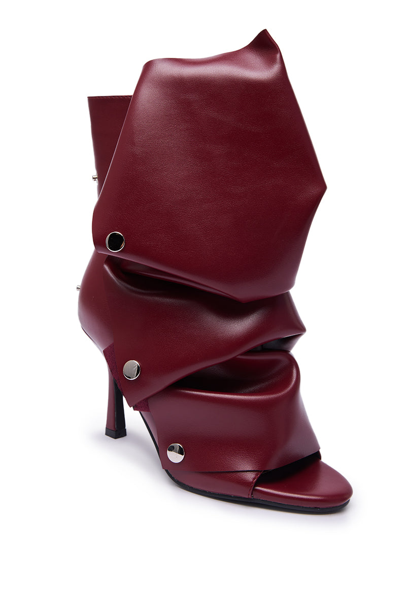 The AZALEA WANG BIRDSONG BURGUNDY SNAP OPEN TOE STILETTO BOOTIE is a high-heeled, avant-garde style with layered, folded panels and bold silver rivets for a sculptural look.