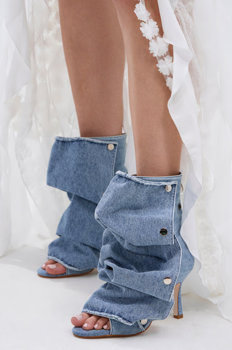 A person wears AZALEA WANG BIRD SONG DENIM OPEN TOE SNAP BOOTIE styled with a white sheer skirt featuring floral appliqués.