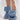A person wears AZALEA WANG BIRD SONG DENIM OPEN TOE SNAP BOOTIE styled with a white sheer skirt featuring floral appliqués.