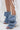 A person wears AZALEA WANG BIRD SONG DENIM OPEN TOE SNAP BOOTIE styled with a white sheer skirt featuring floral appliqués.