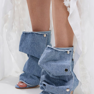 A person wears AZALEA WANG BIRD SONG DENIM OPEN TOE SNAP BOOTIE styled with a white sheer skirt featuring floral appliqués.