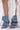 Wearing the AZALEA WANG BIRD SONG DENIM OPEN TOE SNAP BOOTIE—slouchy, oversized denim booties with silver snaps and stiletto heels—a person stands on a white floor, their legs draped in a long, white lace floral garment.