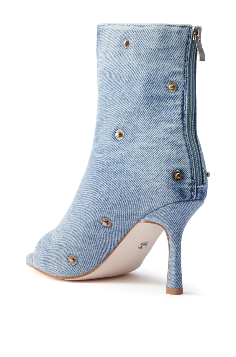 The AZALEA WANG BIRD SONG DENIM OPEN TOE SNAP BOOTIE features a light blue denim finish, metal snap button accents, side zipper, and sleek stiletto heel. Displayed from a side angle on a plain white background.