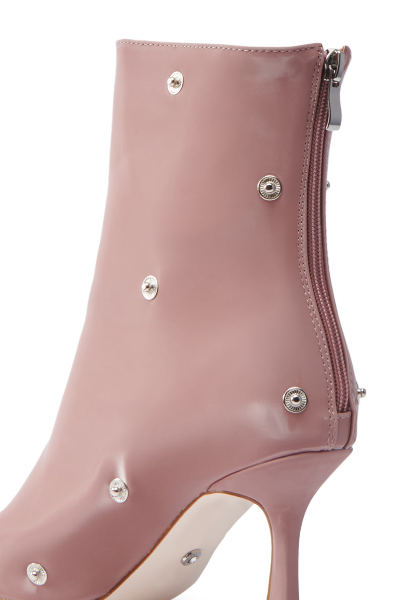 A close-up of the AZALEA WANG BIRD SONG SNAP OPEN TOE BOOTIE in mauve showcases its ultra-stylish stiletto heel, adorned with silver studs. This faux patent leather boot features a glossy finish with a side zipper and pointed toe, making it perfect for making a statement.