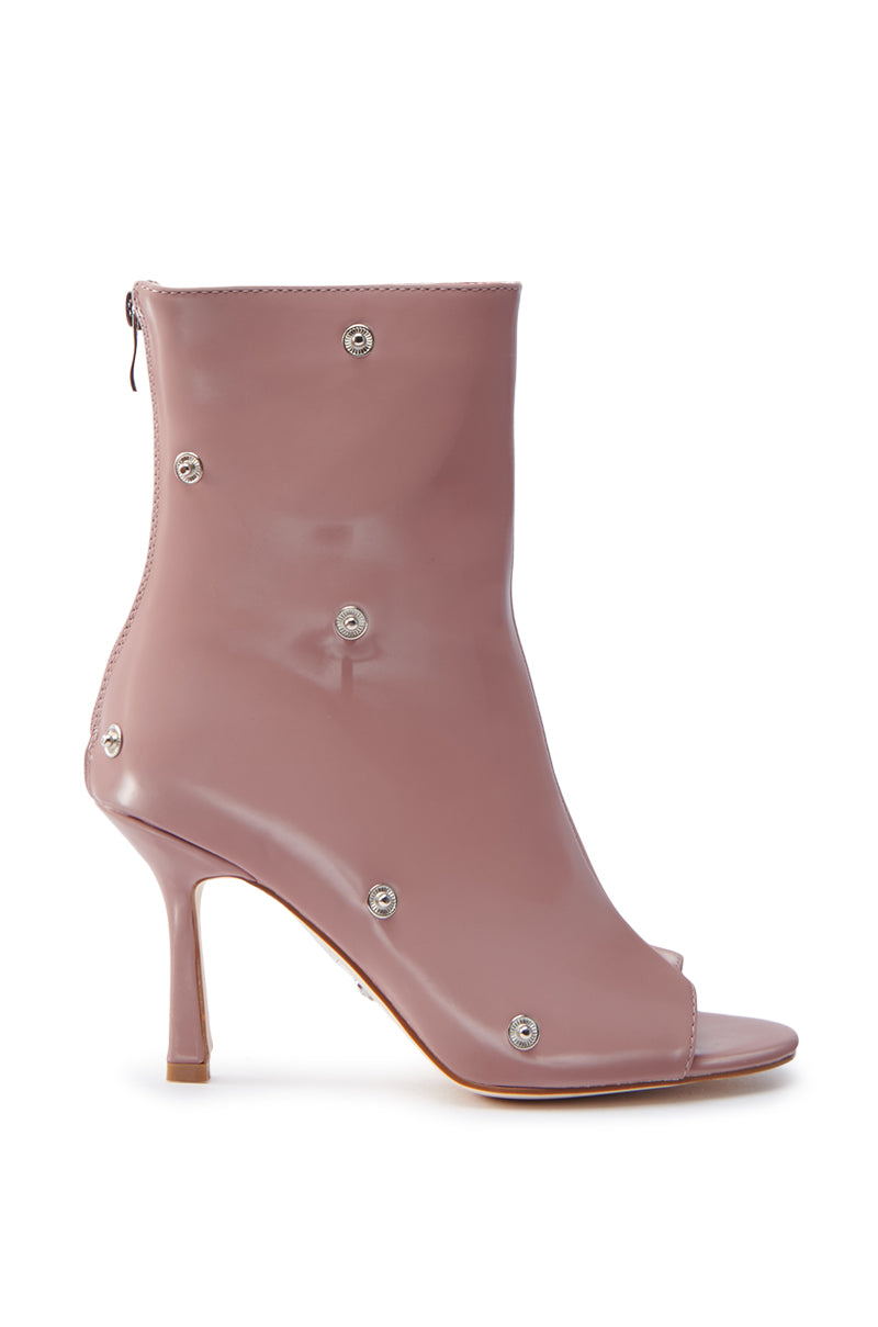 The AZALEA WANG BIRD SONG SNAP OPEN TOE BOOTIE in mauve is a shiny, light purple faux patent leather ankle boot with a peep toe, stiletto heel, circular silver studs, and rear zipper closure.