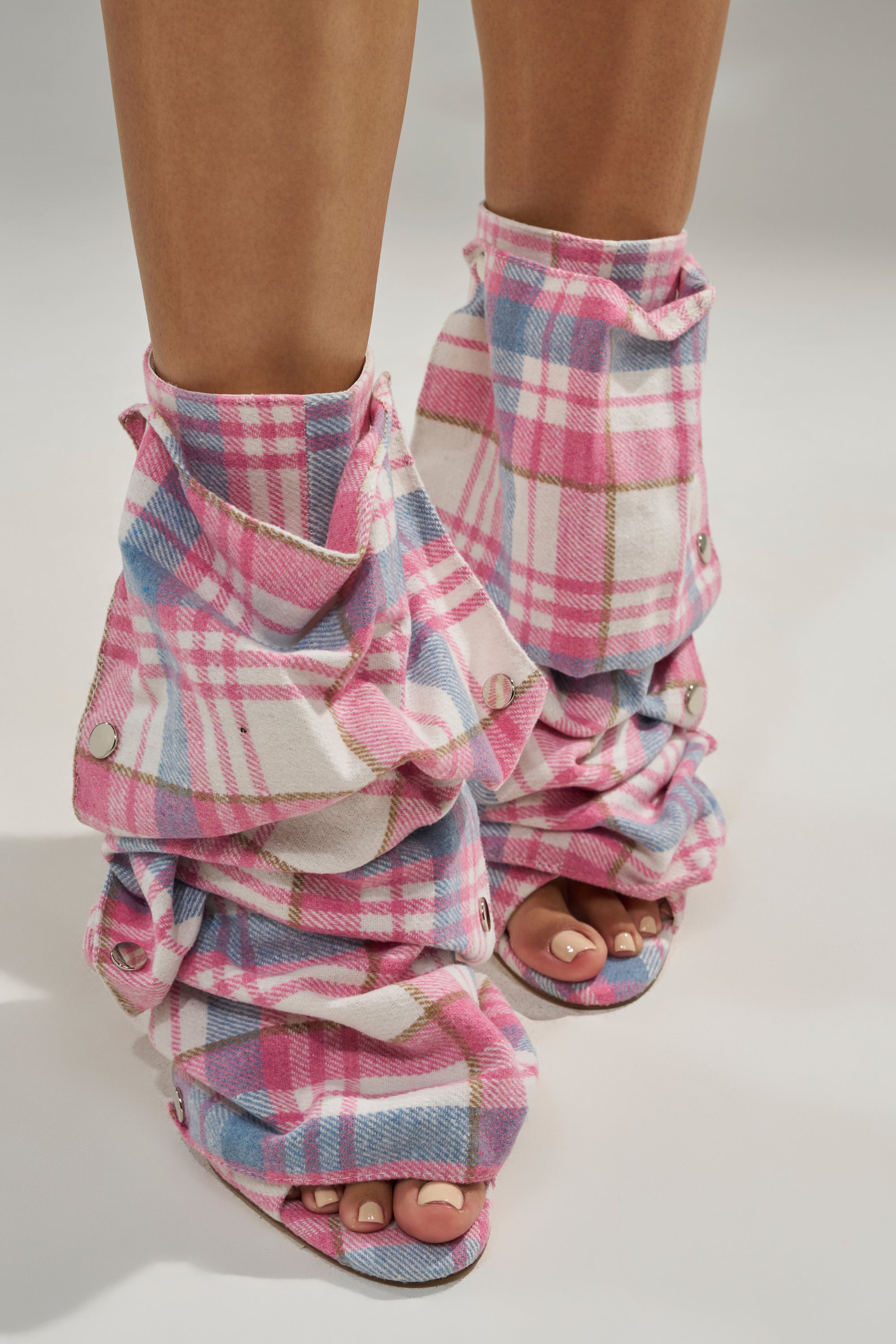 Close-up of feet in the AZALEA WANG BIRD SONG PINK PLAID MULTI OPEN TOE SNAP BOOTIE, wrapped with layered pink plaid fabric extending to mid-calf for a ruched effect. Light pink toenails complete the look.