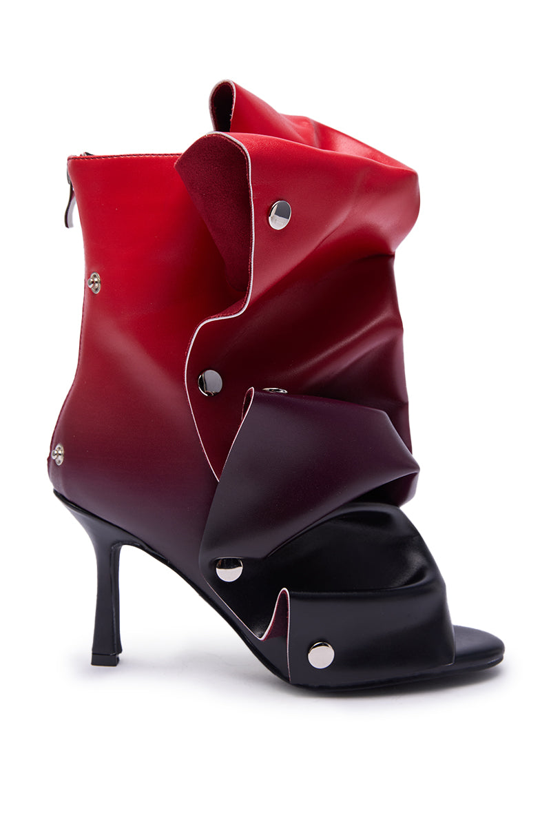 The AZALEA WANG BIRDSONG RED OMBRE SNAP OPEN TOE BOOTIE features a high stiletto heel, sculptural folded red and black faux leather design, silver snap accents, open toe, and back zipper.
