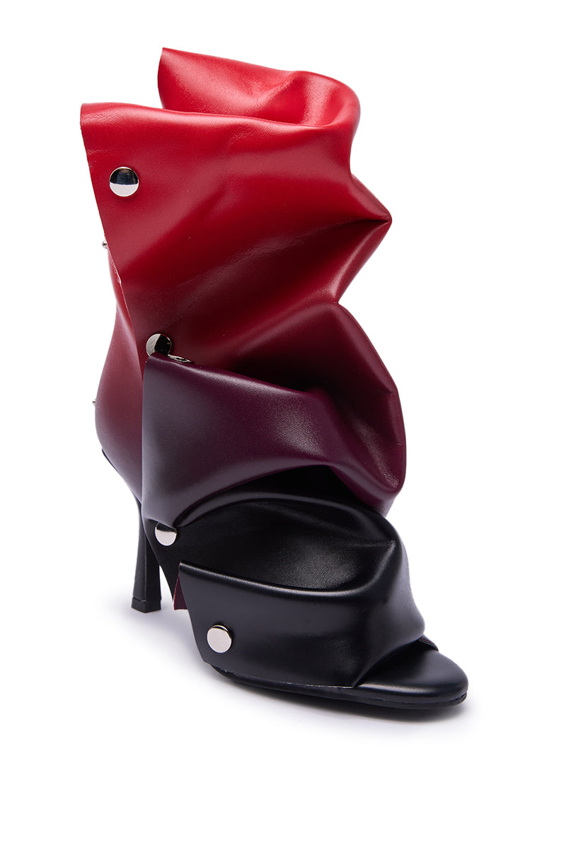 The AZALEA WANG BIRDSONG RED OMBRE SNAP OPEN TOE BOOTIE features an abstract, sculptural design with layered black and deep red faux leather, silver studs, and a bold avant-garde open toe style for a dramatic edge.