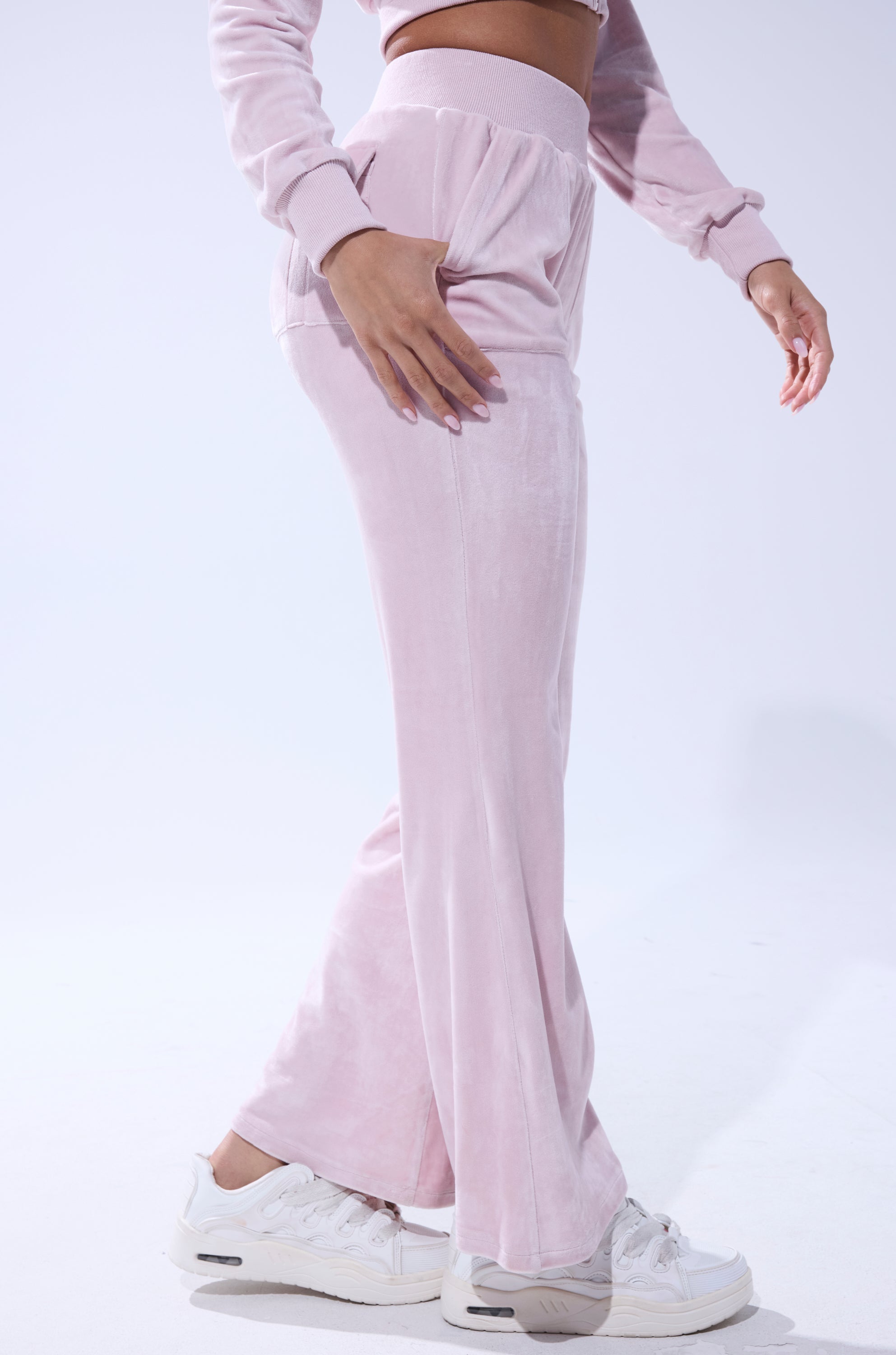 A person models the TAYLOR STRAIGHT LEG JOGGER IN PINK with a matching top and white sneakers against a plain white background, one hand on their hip and the other by their side. 4