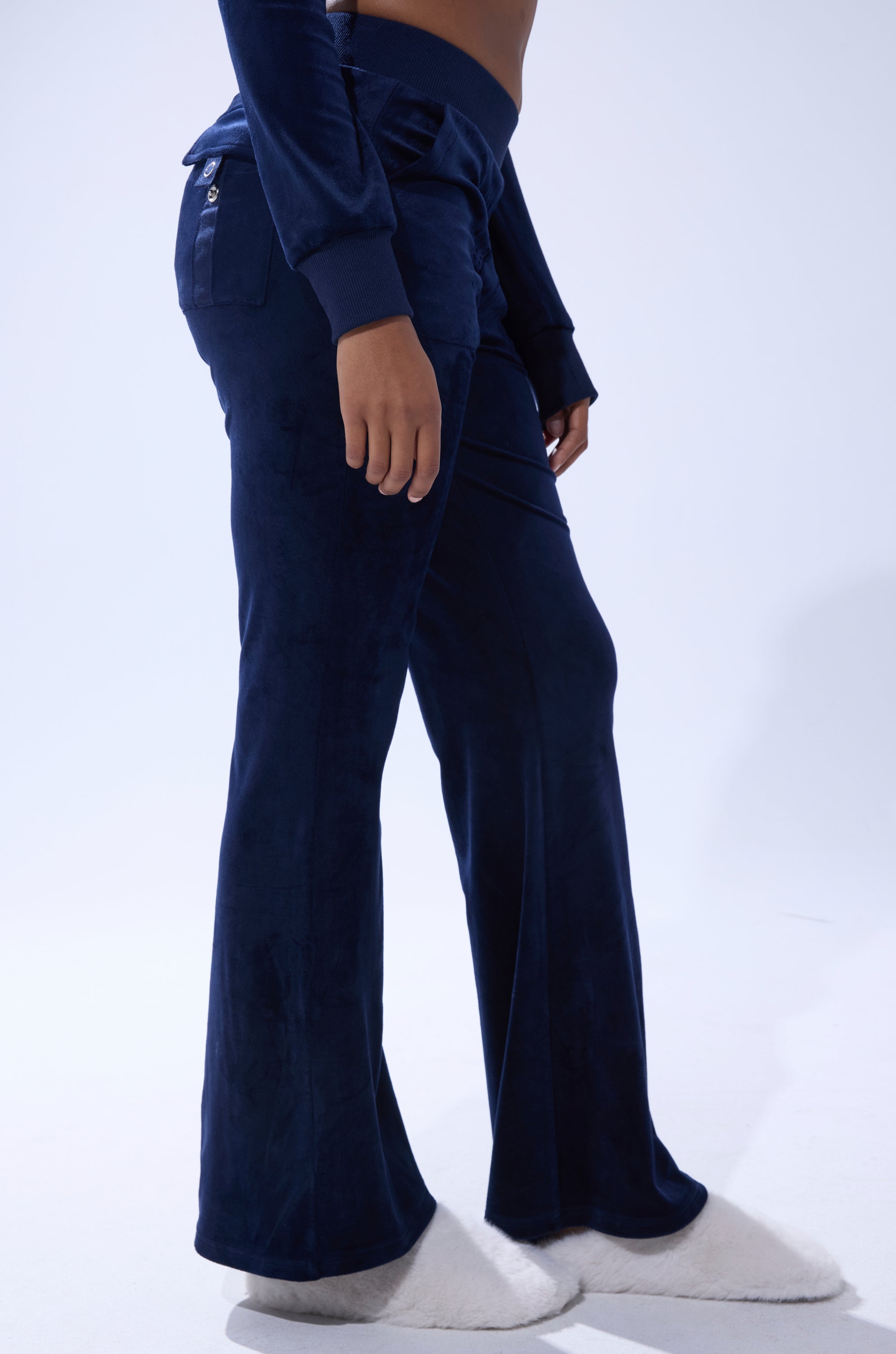 A person wearing the TAYLOR STRAIGHT LEG JOGGER IN NAVY, a matching top, and white fuzzy slippers stands against a plain light background. 2
