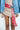 A person in a beige ribbed dress and denim jacket wears the striking ROSES ARE RED CIRCLE BELT, featuring large red circular metallic pieces and a prominent silver buckle. Their outfit, rich in silver details, is completed by gray high boots.