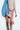 A person in a beige ribbed dress draped with a denim jacket over one shoulder wears the Western-inspired "ROSES ARE RED CIRCLE BELT" with circular patterns and a silver buckle, along with knee-high snakeskin boots featuring subtle silver details.
