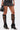 Only the lower body is visible: a person in a short dark skirt and black AZALEA WANG BLACKBIRD PU stiletto gladiator sandals with straps and buckles, holding a small black handbag.