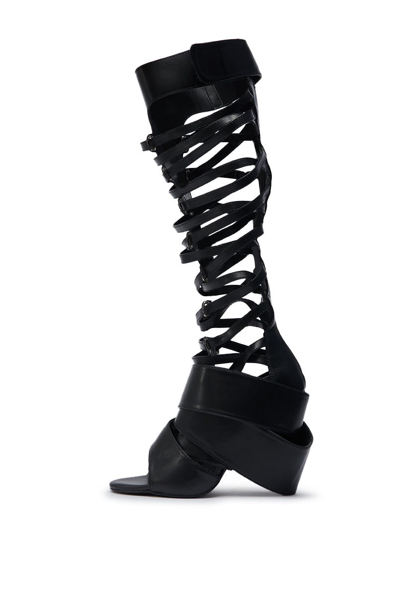 The AZALEA WANG BLACKBIRD BLACK PU STILETTO GLADIATOR SANDAL is a single black faux leather knee-high with multiple crisscross straps, an open toe, and a thick angled heel, shown on a white background.