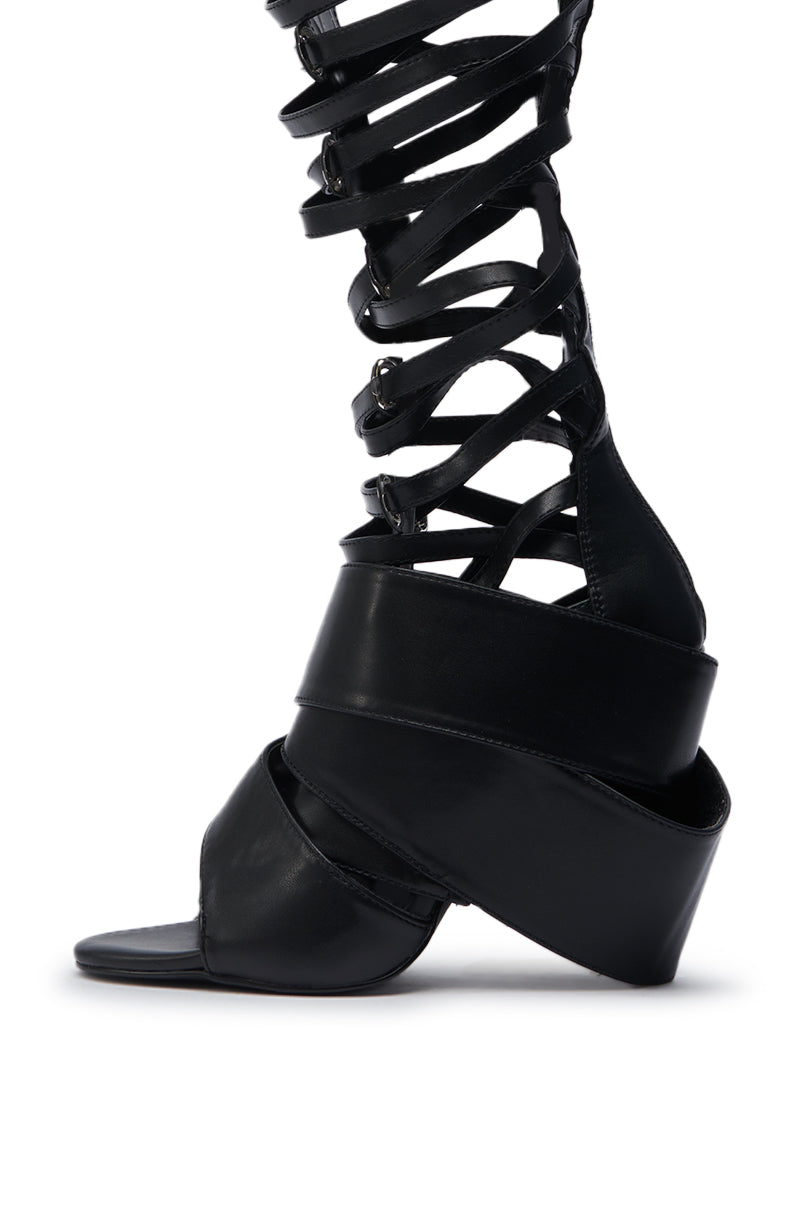 The AZALEA WANG BLACKBIRD BLACK PU STILETTO GLADIATOR SANDAL features multiple black straps, an open toe, and knee-high style with a sleek stiletto heel, displayed against a white background.