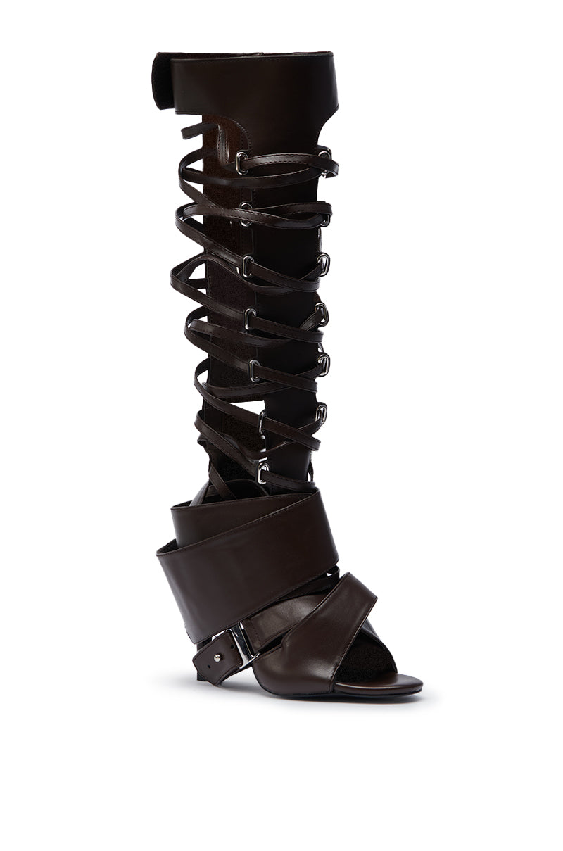 The AZALEA WANG BLACKBIRD BROWN PU STILETTO GLADIATOR SANDAL features knee-high crisscross straps, chunky ankle accents, metal eyelets, a stiletto heel, and an open toe for standout style.
