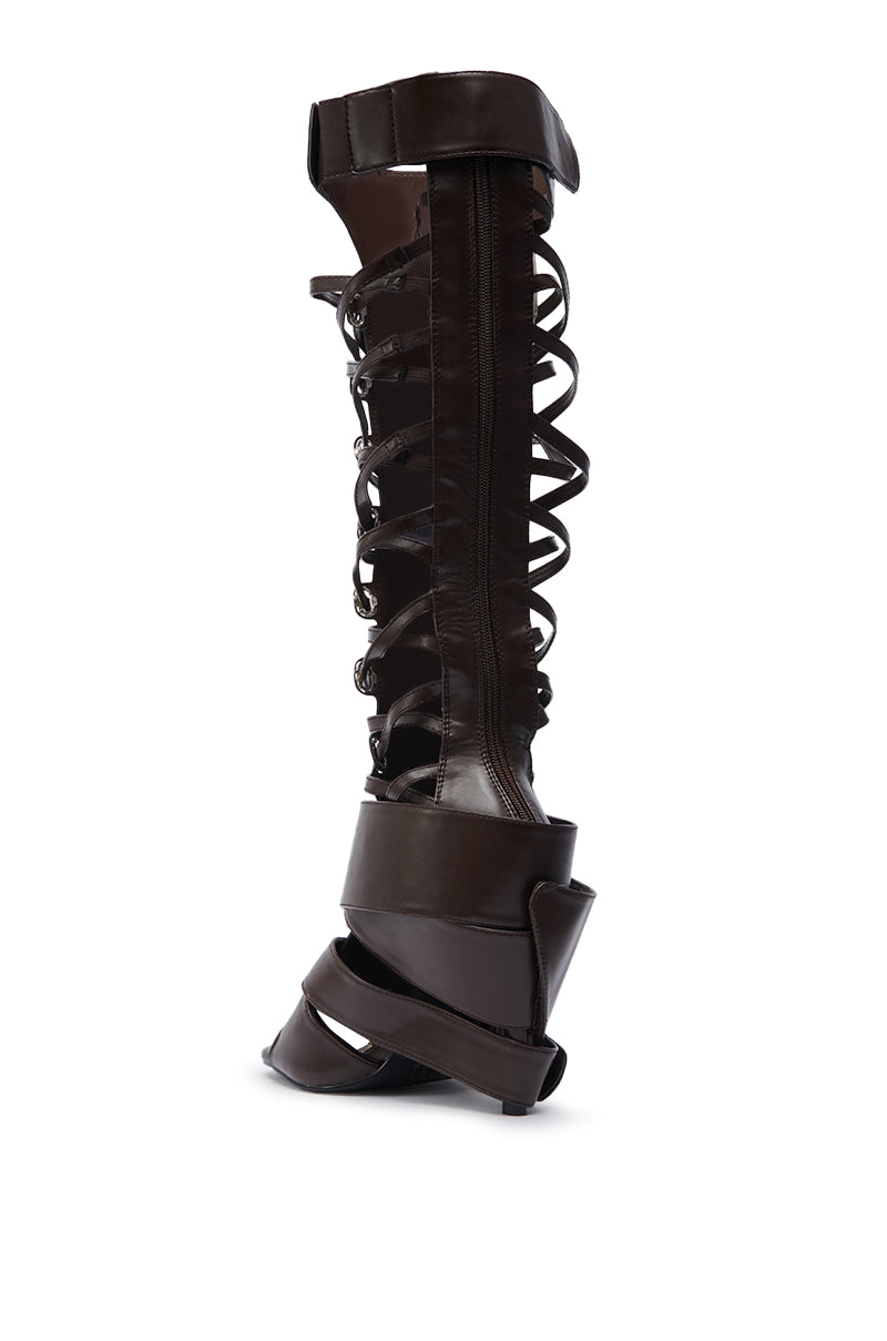 The AZALEA WANG BLACKBIRD BROWN PU STILETTO GLADIATOR SANDAL features knee-high dark faux leather, intricate cutouts, crisscross straps, and a bold sculptural platform—an elevated spin on the classic gladiator sandal.