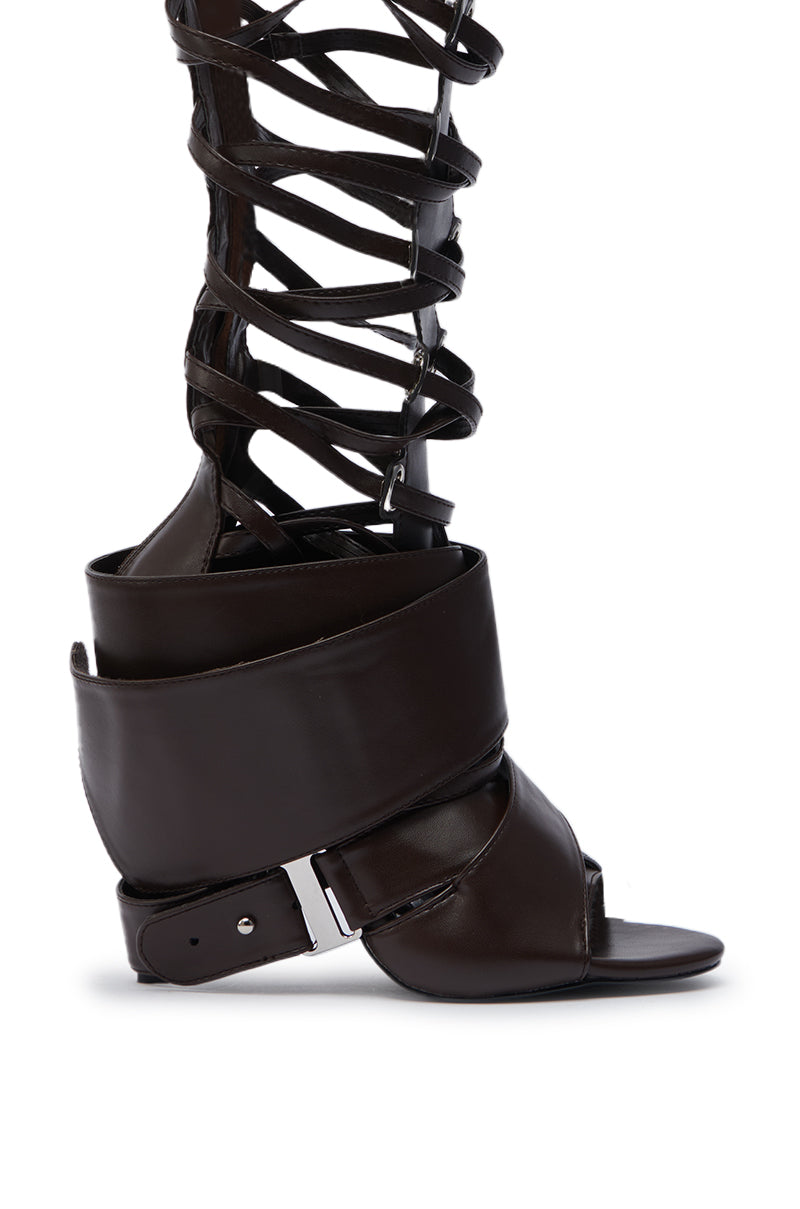 The AZALEA WANG BLACKBIRD BROWN PU STILETTO GLADIATOR SANDAL features luxe faux leather, high crisscross straps, and a wide silver-buckled cuff, making a bold statement against a crisp white background.