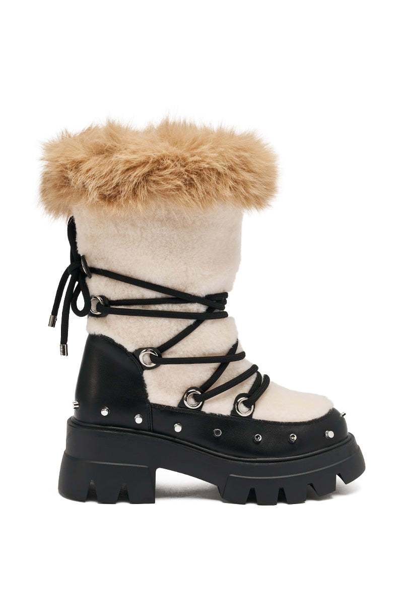 The AZALEA WANG BLEJAN BLACK FUR AND SHERPA BOOTIE features a chunky black sole, cream-colored shearling upper, tan faux fur trim, and black laces with metal eyelets and stud accents wrapping around the boot.