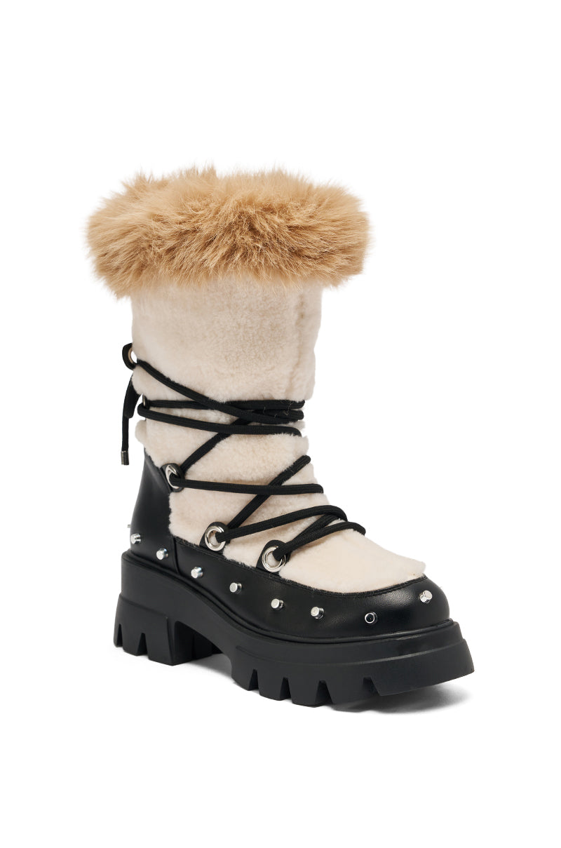 The AZALEA WANG BLEJAN BLACK FUR AND SHERPA BOOTIE features a chunky black sole, cream suede upper, tan faux sherpa trim, black leather accents, silver rivets, and black crisscross laces wrapped around the boot.