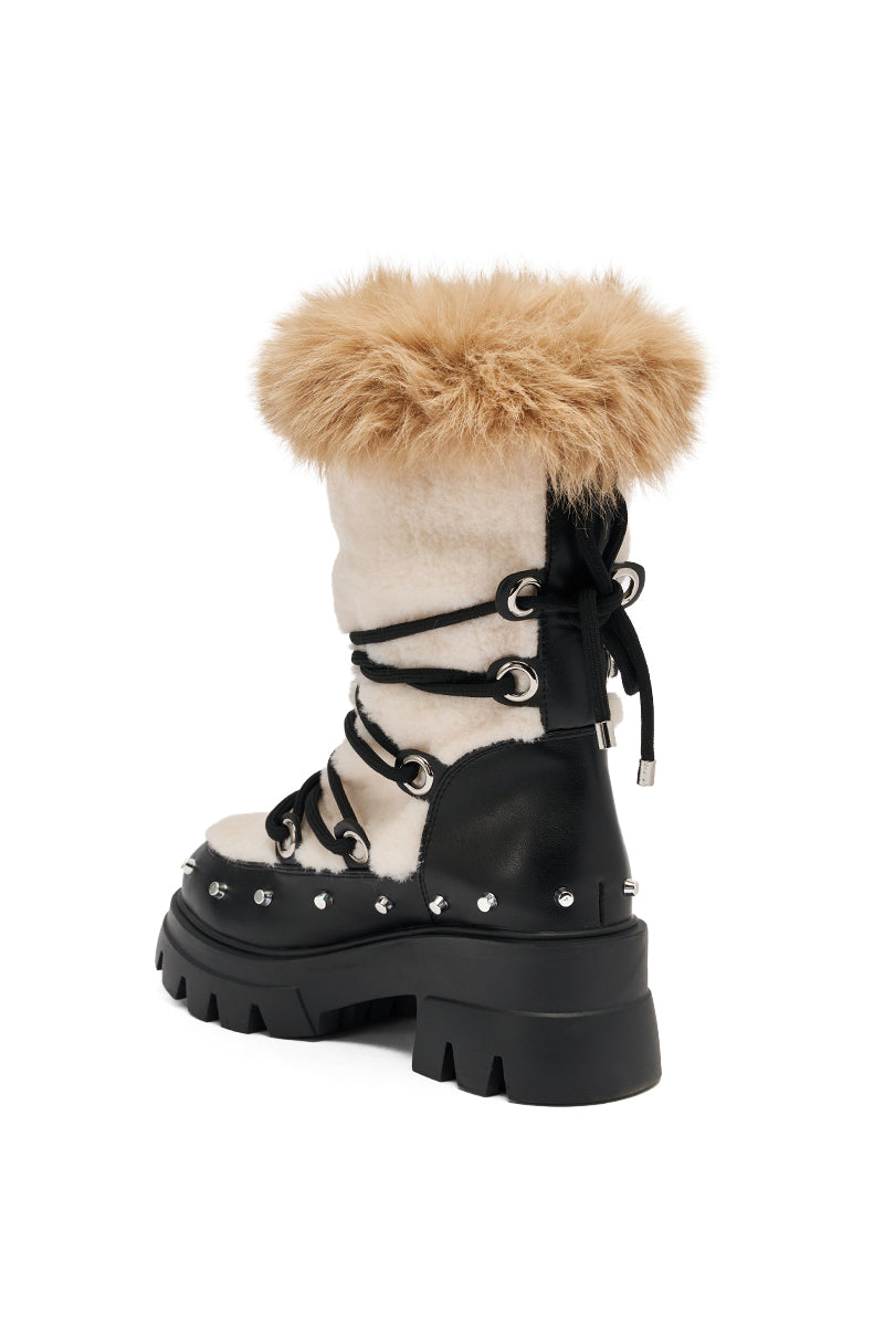 The AZALEA WANG BLEJAN BLACK FUR AND SHERPA BOOTIE features a white faux sherpa upper, chunky lug sole, black leather accents, silver studs, black laces, and a tan faux fur cuff for a stylish look.