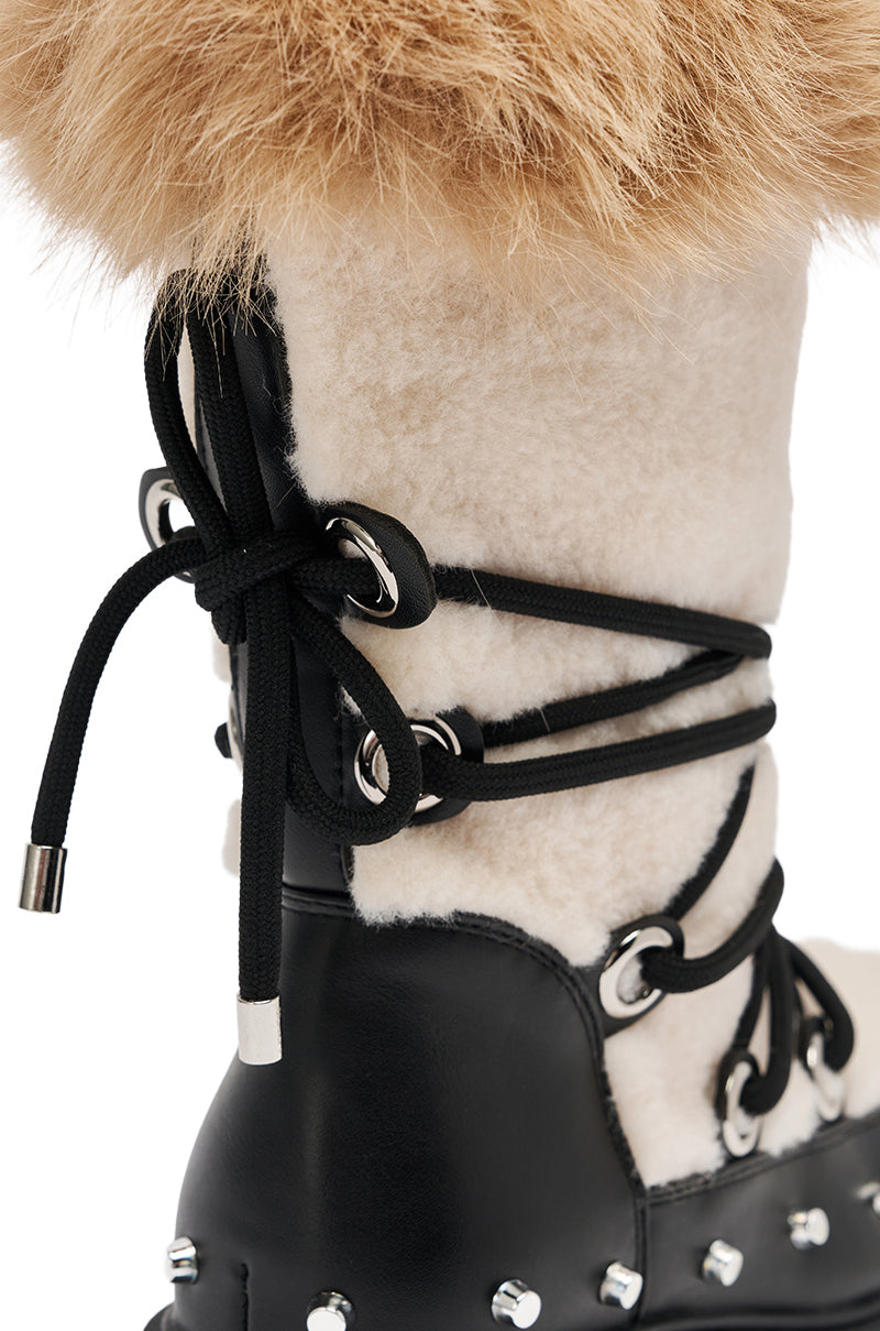 The AZALEA WANG BLEJAN BLACK FUR AND SHERPA BOOTIE features a black fur finish, white faux sherpa details, black leather accents, chunky lug sole, black laces through silver eyelets, tan fur trim at the top, and silver studs along the sole.