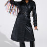Someone wearing the RYDER FRINGE TRENCH IN BLACK MULTI with colorful fringe sleeves, matching lace-up pants, a black cowboy hat with silver details, glasses, and pointed boots.