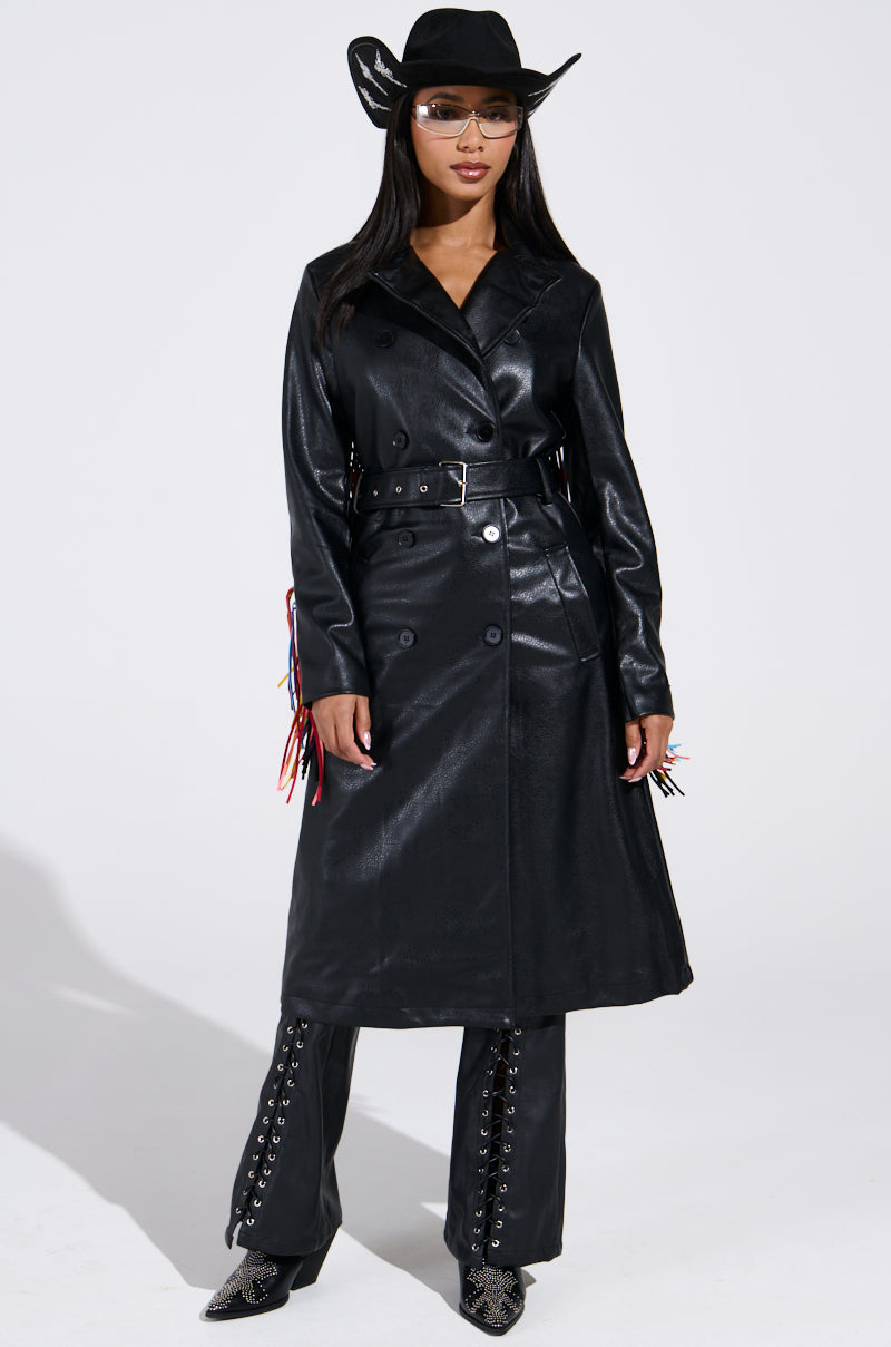 A woman models the RYDER FRINGE TRENCH IN BLACK MULTI, showcasing multi-color fringe and pebbled faux leather, paired with black pants, a cowboy hat, and sunglasses against a white background.