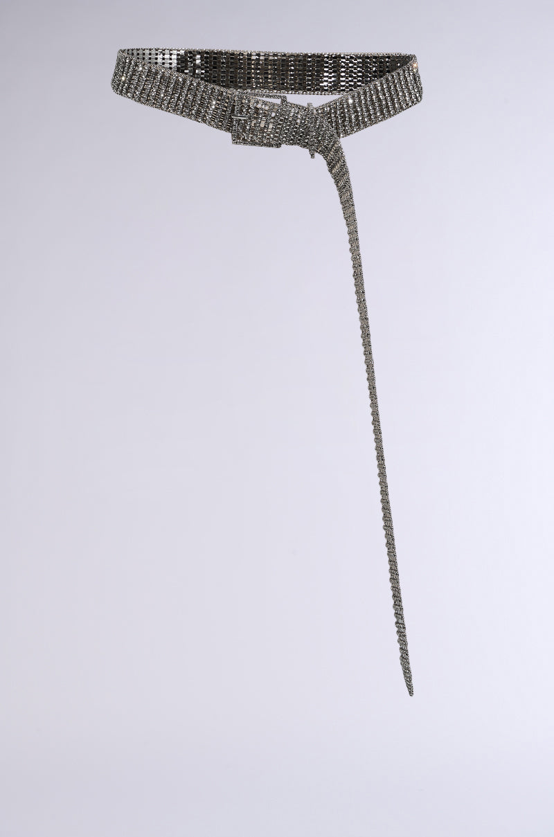 The RHINESTONE BELT is a silver mesh design with a long, dangling end set against a plain, light background. Featuring silver hardware and a rectangular buckle, it shines with an elegant metallic sheen. 2