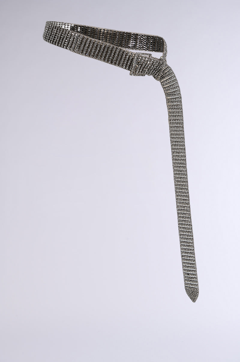 The RHINESTONE BELT is a silver mesh chain with rhinestones, featuring a slim design and a looped knot creating a long, dangling tail. Its textured pattern and sparkling embellishments beautifully catch the light against a plain gray background. 3