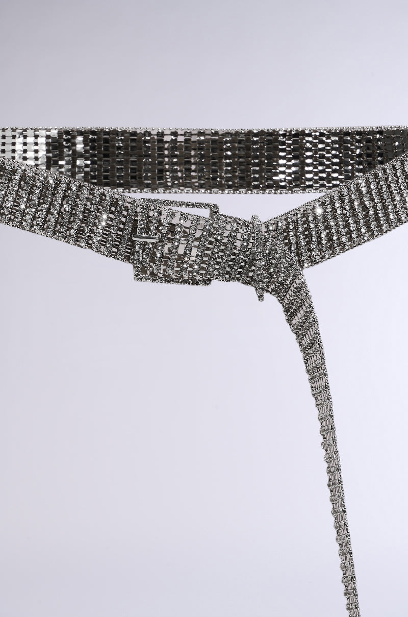 The Rhinestone Belt is a shiny silver waist-cinching accessory made of interlocking metallic squares, featuring a rectangular buckle, displayed diagonally on a plain gray background. 4