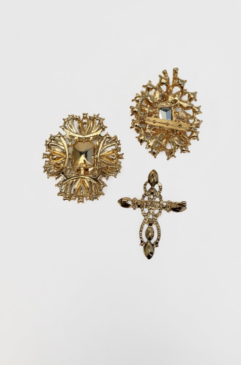 The ULTIMATE BROOCH SET includes three gold brooches: two with symmetrical, jeweled designs and one cross-shaped rhinestone brooch, all presented on a plain white background.