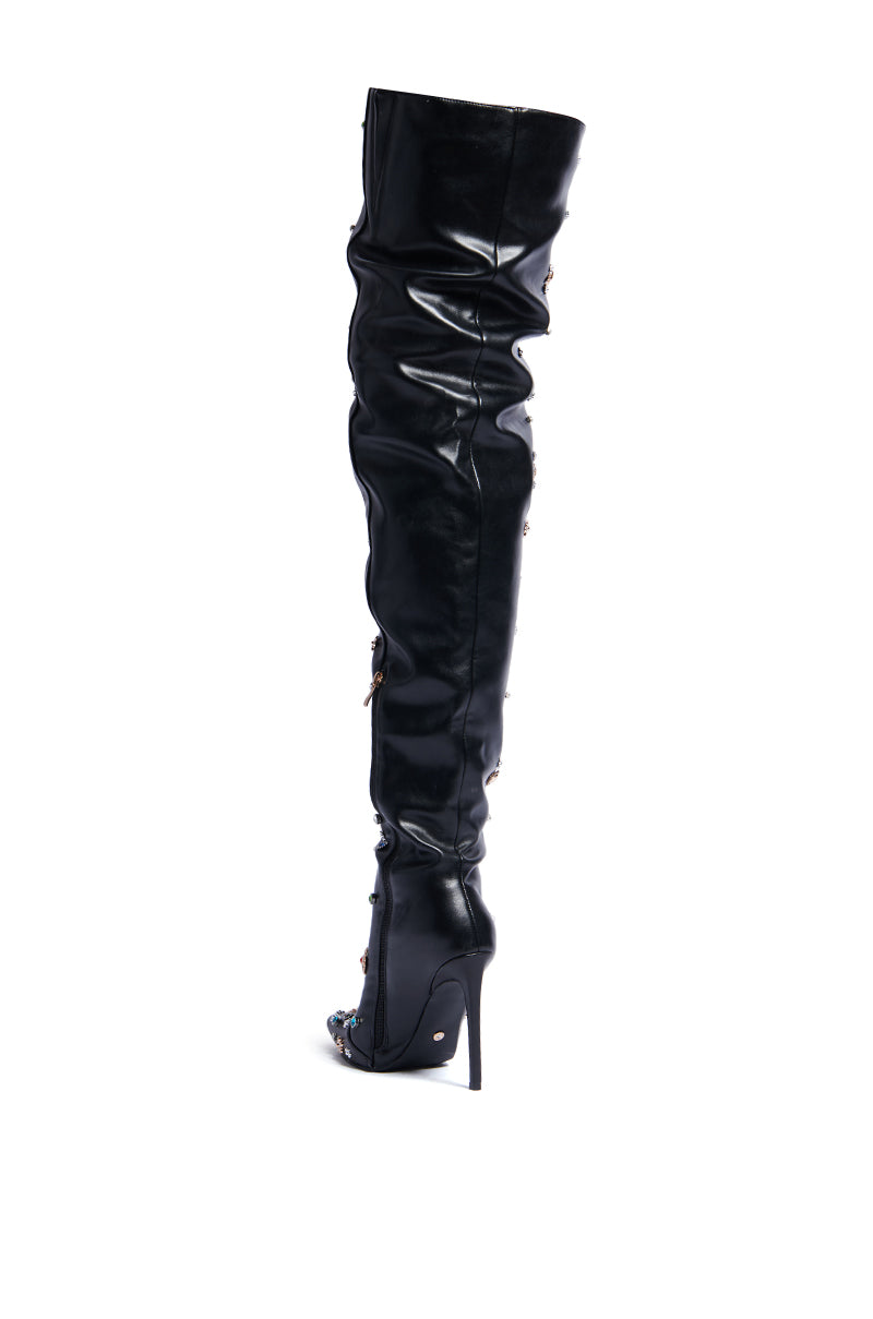 Introducing the AZALEA WANG BOBEE BLACK EMBELLISHED BOOT, a stunning black thigh-high stiletto crafted from luxurious faux leather. This boot boasts a pointed toe and shiny finish, complemented by decorative side details. The slender, tall heel accentuates its sleek and stylish design. 4