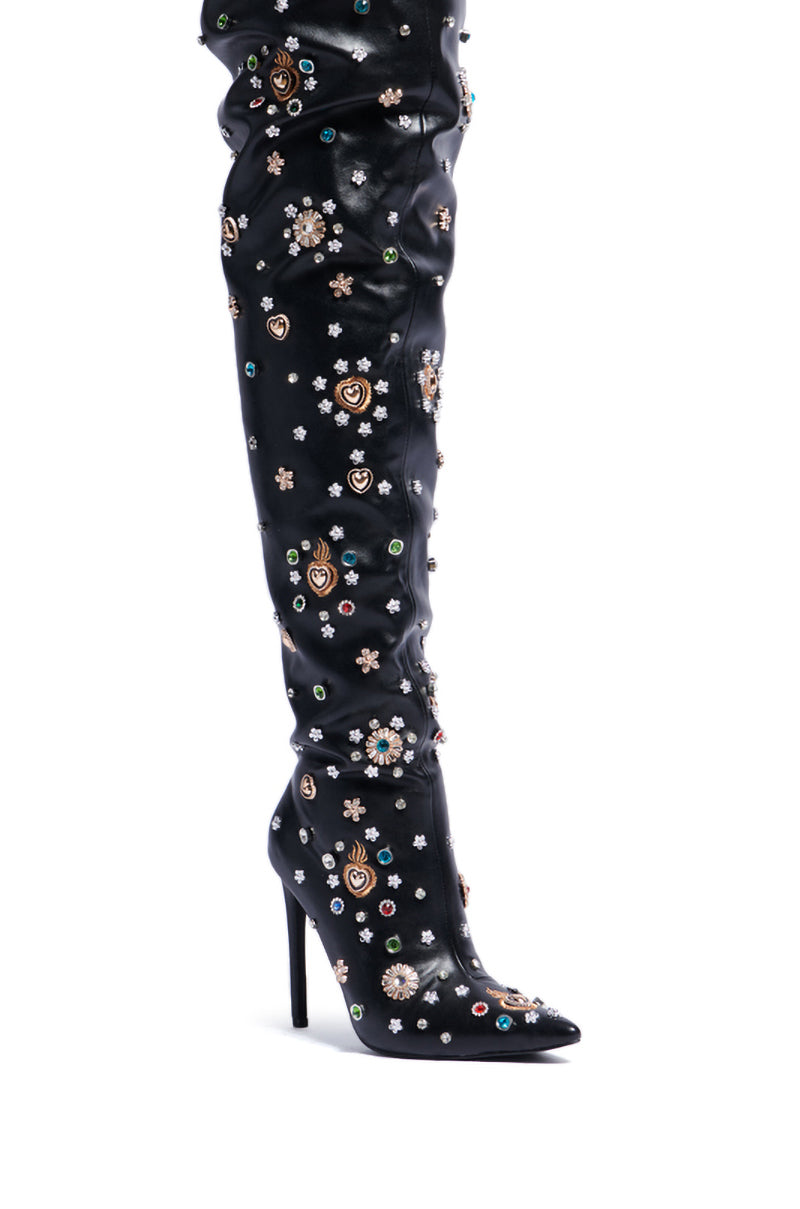 A close-up of the AZALEA WANG BOBEE BLACK EMBELLISHED BOOT reveals its striking faux leather thigh-high style, featuring a high stiletto heel and adorned with multicolored gems and decorative floral patterns. This intricate design makes a luxurious and bold fashion statement. 5