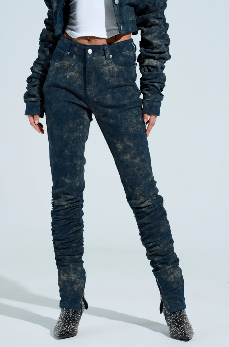 A person in the UNFORGETTABLE STACKED PANT, a matching acid wash jacket, and white top. They're also sporting textured ankle boots against a light blue backdrop.