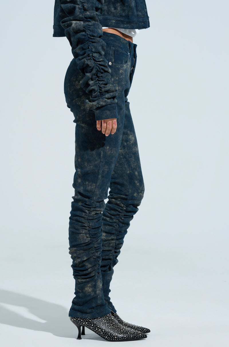 A person wearing a matching denim jacket and UNFORGETTABLE STACKED PANT set in dark blue acid wash denim, featuring ruching on sleeves and legs for a stacked look. They pair the outfit with pointed, studded black heeled boots.