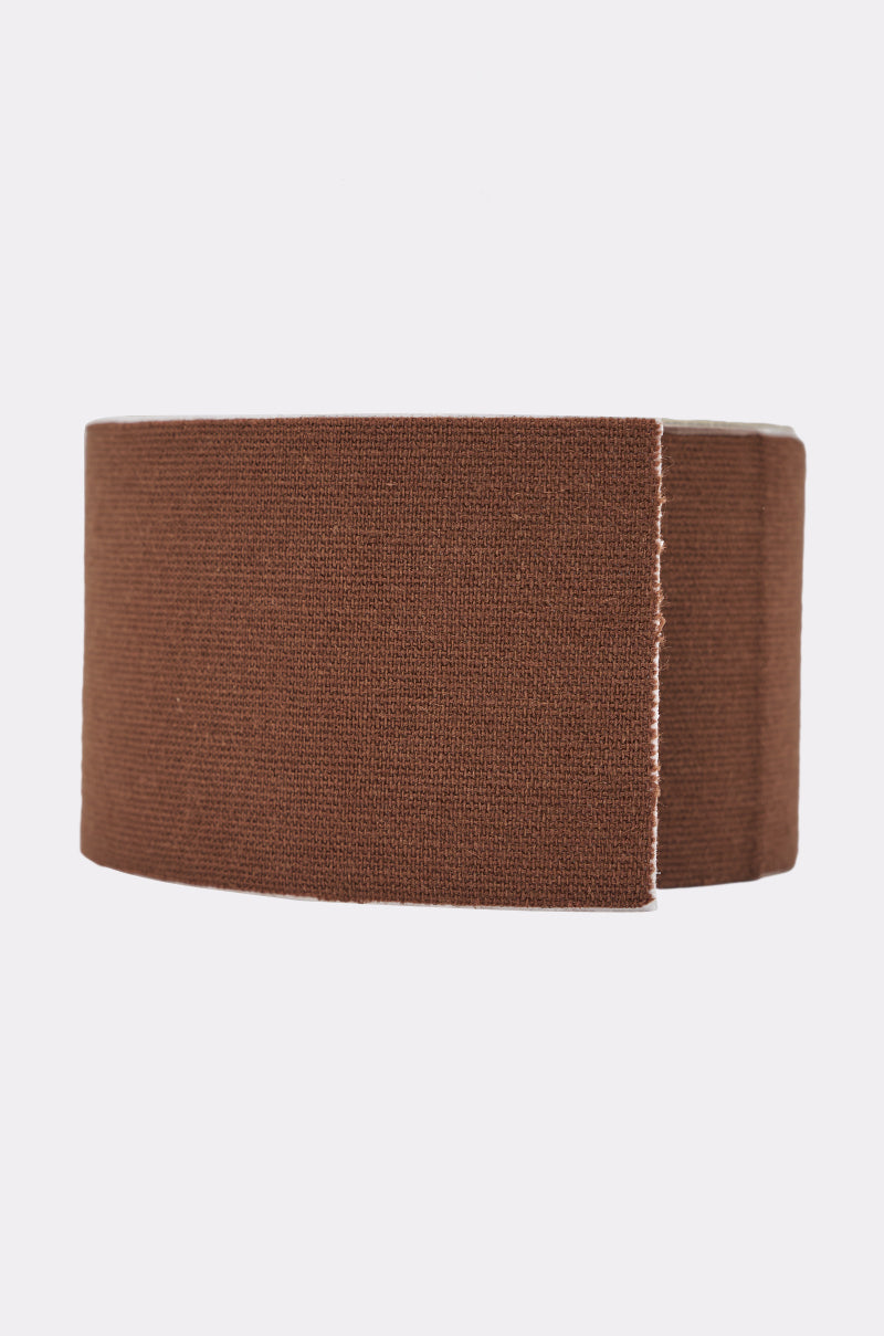 A roll of TITSY ULTRA LIFT BOOB TAPE IN DARK, a brown, textured elastic trimming ideal as discreet lift boob tape for backless outfits, with one end slightly unrolled against a plain light background. 1