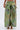 A person wearing PEACOCK TROUSER pants featuring a metallic green, yellow, and purple feather pattern with large cargo pockets and gold sandal heels; upper torso not visible.