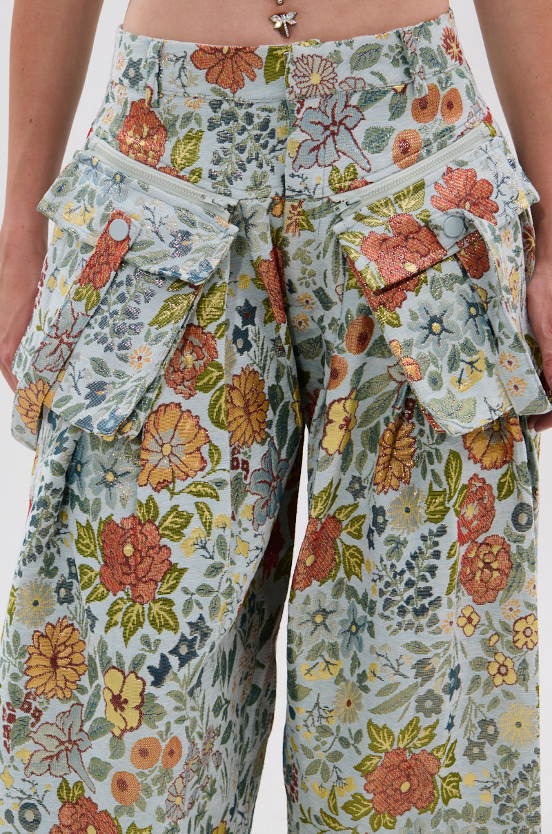 A close-up of a person wearing MARTHA FLORAL CARGO PANTS—high-waisted, wide-leg jacquard cargo pants with large side pockets, white zippers, orange accents, and a butterfly belly button piercing. 5
