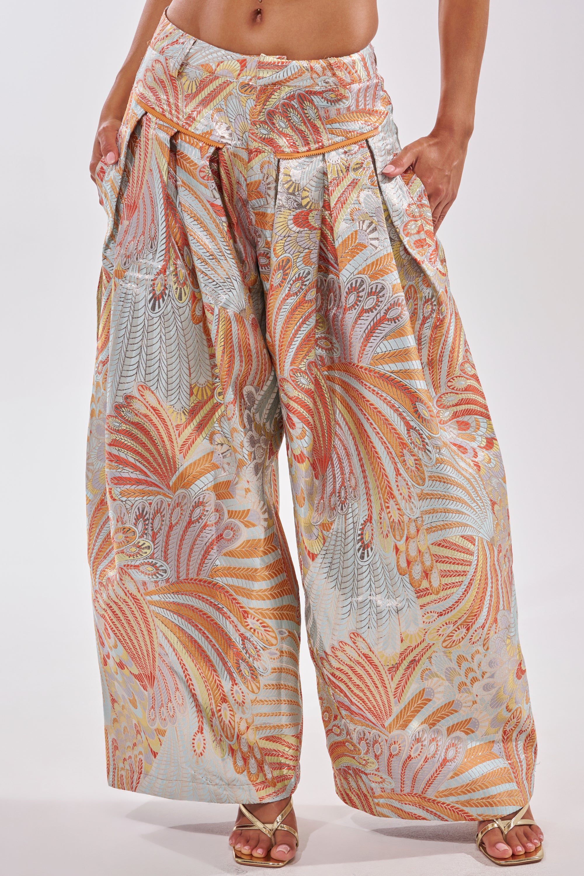 Someone is wearing the MARTHA FLORAL TROUSER: blue wide-leg pants featuring a vibrant feather and leaf pattern in orange, pink, and light blue tones, styled with heeled sandals. 8