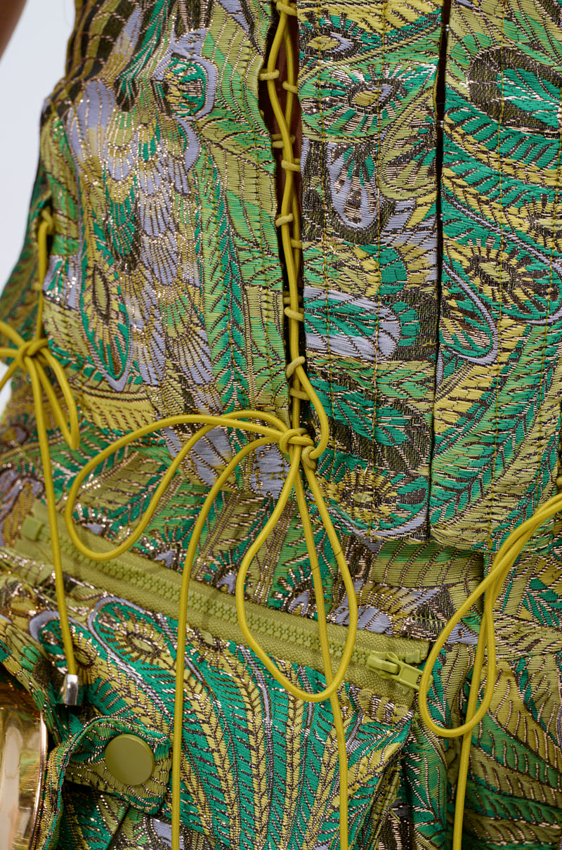 Close-up of the PEACOCK CORSET, showcasing intricate green, gold, and blue embroidery with yellow cord lacing and decorative knots that highlight the textured fabric and detailed design.
