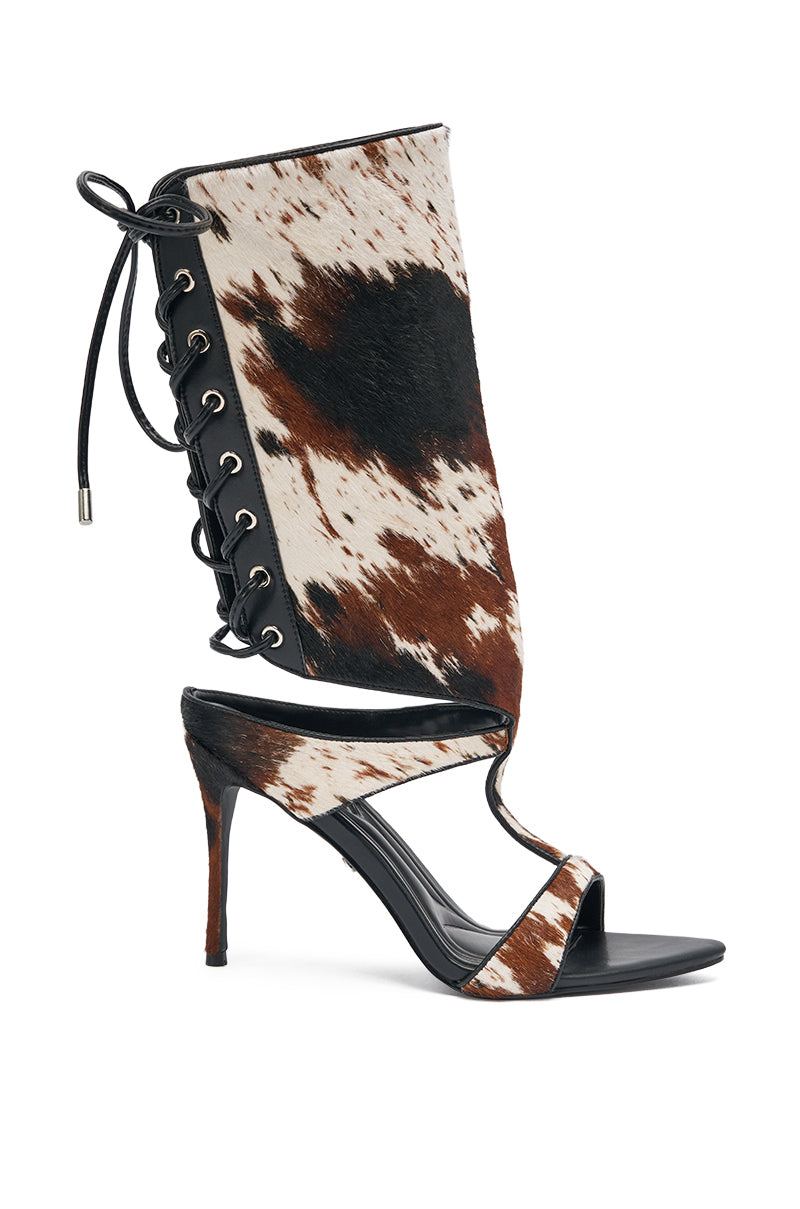 The AKIRA GOLD CALF HAIR LACE UP GLADIATOR STILETTO SANDAL features a black sole, stiletto heel, brown and white cow print upper, lace-up side details, and an open toe design. 3