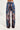 A person is wearing the vibrant DREAMING ABOUT YOU PANT with a high-rise waist, featuring an intricate paisley pattern in shades of blue, purple, brown, and beige. The wide-leg pants stand out against a plain, light-colored background.