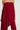 A person is wearing the strapless, flowing, red TARAJI KNIT JUMPSUIT by AKIRA Label. The image emphasizes the upper body, highlighting the super stretchy fabric's texture and drape. The background is plain and light-colored.