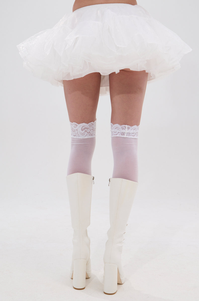 A person stands with their back to the camera in a festival-ready look, featuring the JENNY TULLE MINI SKIRT, white lace-topped thigh-high stockings, and knee-high white block-heel boots against a plain white background. 3