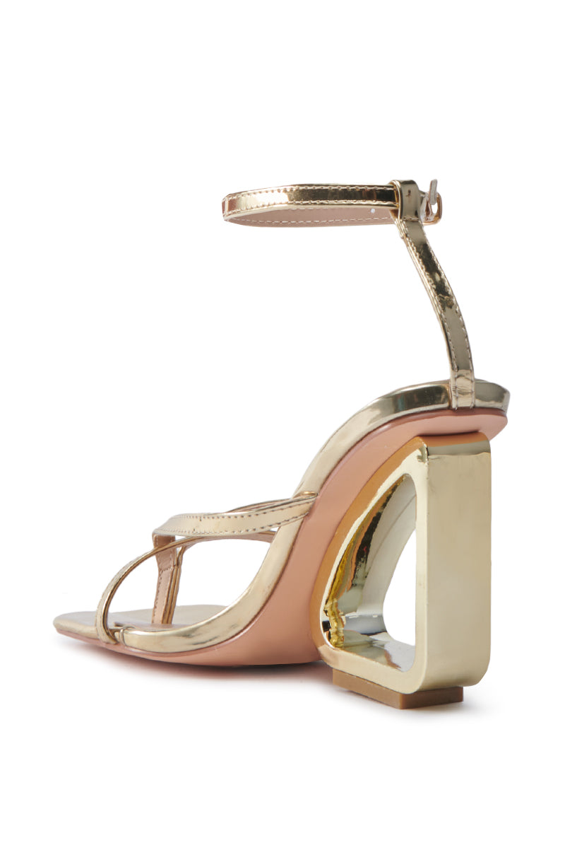 The AKIRA BRANWEN GOLD WEDGE SANDAL is a stylish gold high-heeled sandal featuring a unique geometric cut-out wedge heel, square-toe silhouette, and slim ankle strap. Its minimalist design highlights a glossy finish for a modern look.