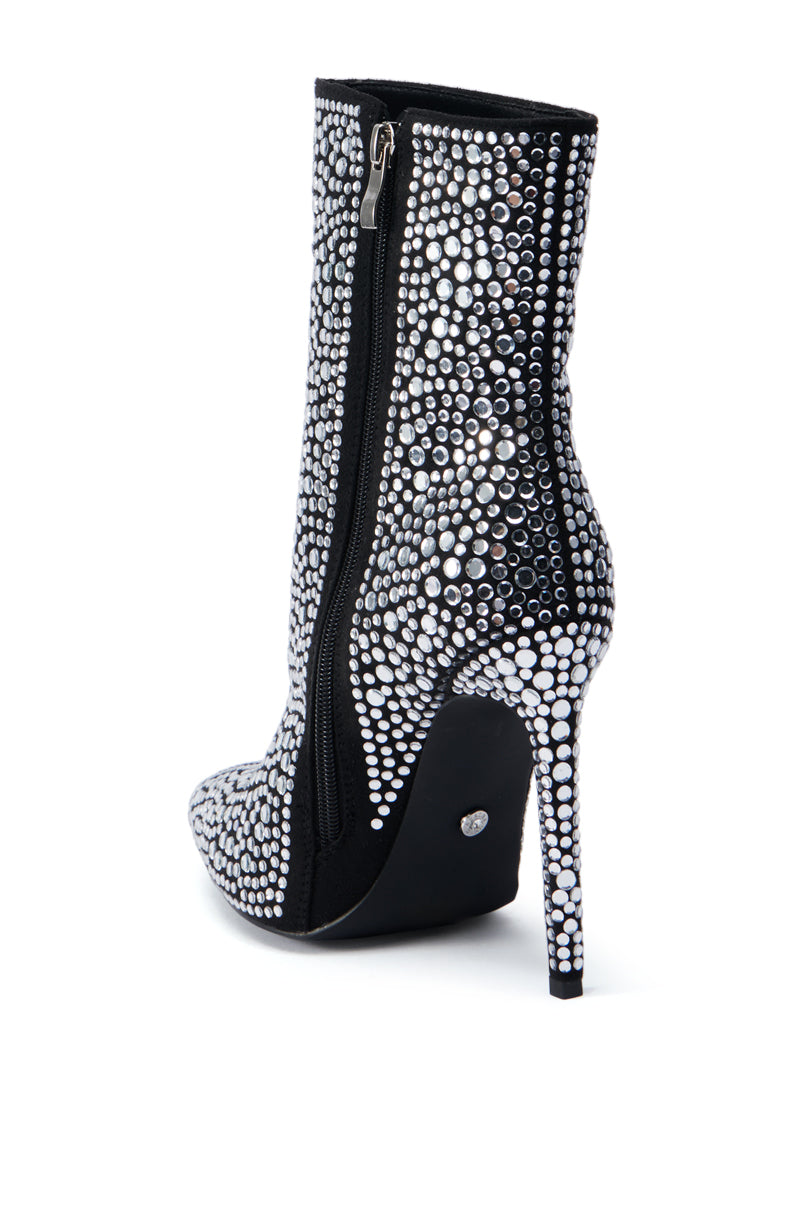The AZALEA WANG BRAULIO BLACK STILETTO BOOTIE is adorned with sparkling rhinestone embellishments on a black faux suede base. This shoe showcases a pointed toe, side zipper, and a stiletto heel encrusted with rhinestones.