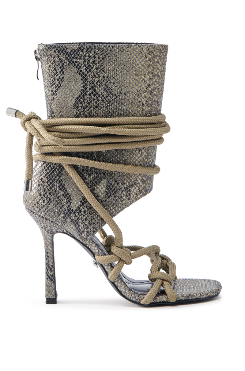 The AZALEA WANG BREELEE SNAKE COCKTAIL BOOTIE is a high-heeled shoe featuring a snakeskin pattern with an ankle-high, pointed opening, beige rope elegantly wrapped around the ankle forming decorative knots along the front, and a sleek stiletto heel.