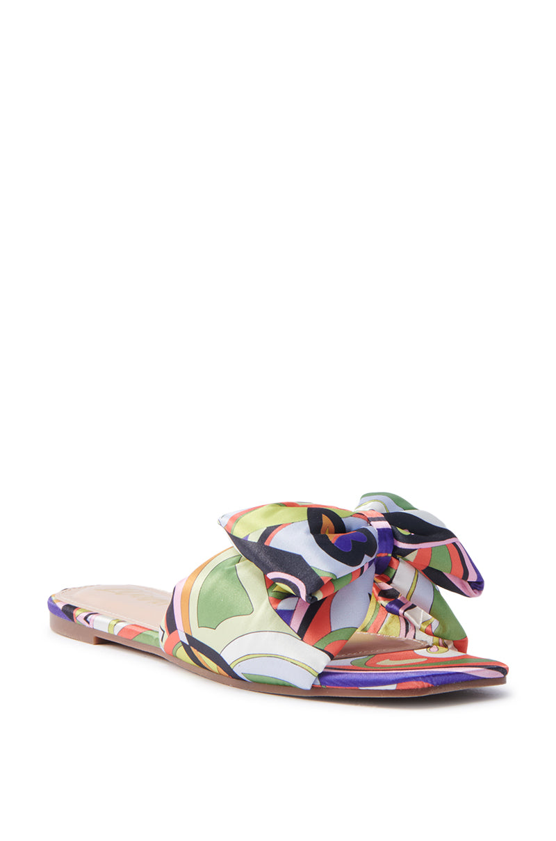 The BREEZY SCARF FLAT SANDAL IN CHARTREUSE showcases a vibrant, abstract swirl design in green, pink, orange, and black with a wide bow on the front and simple flat sole, adding playful elegance to any outfit.